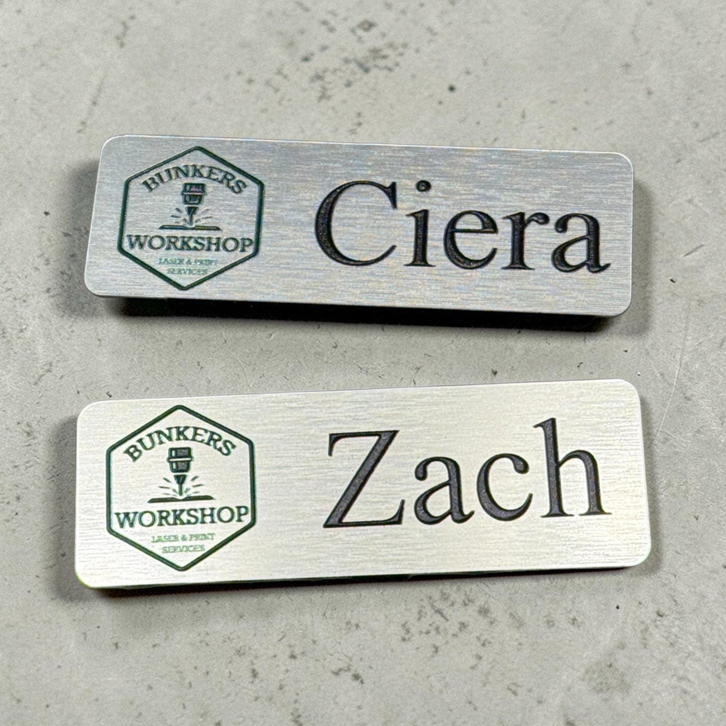 Custom brushed silver metal name badge with personalized logo, magnetic or pin back, by Bunkers Workshop.