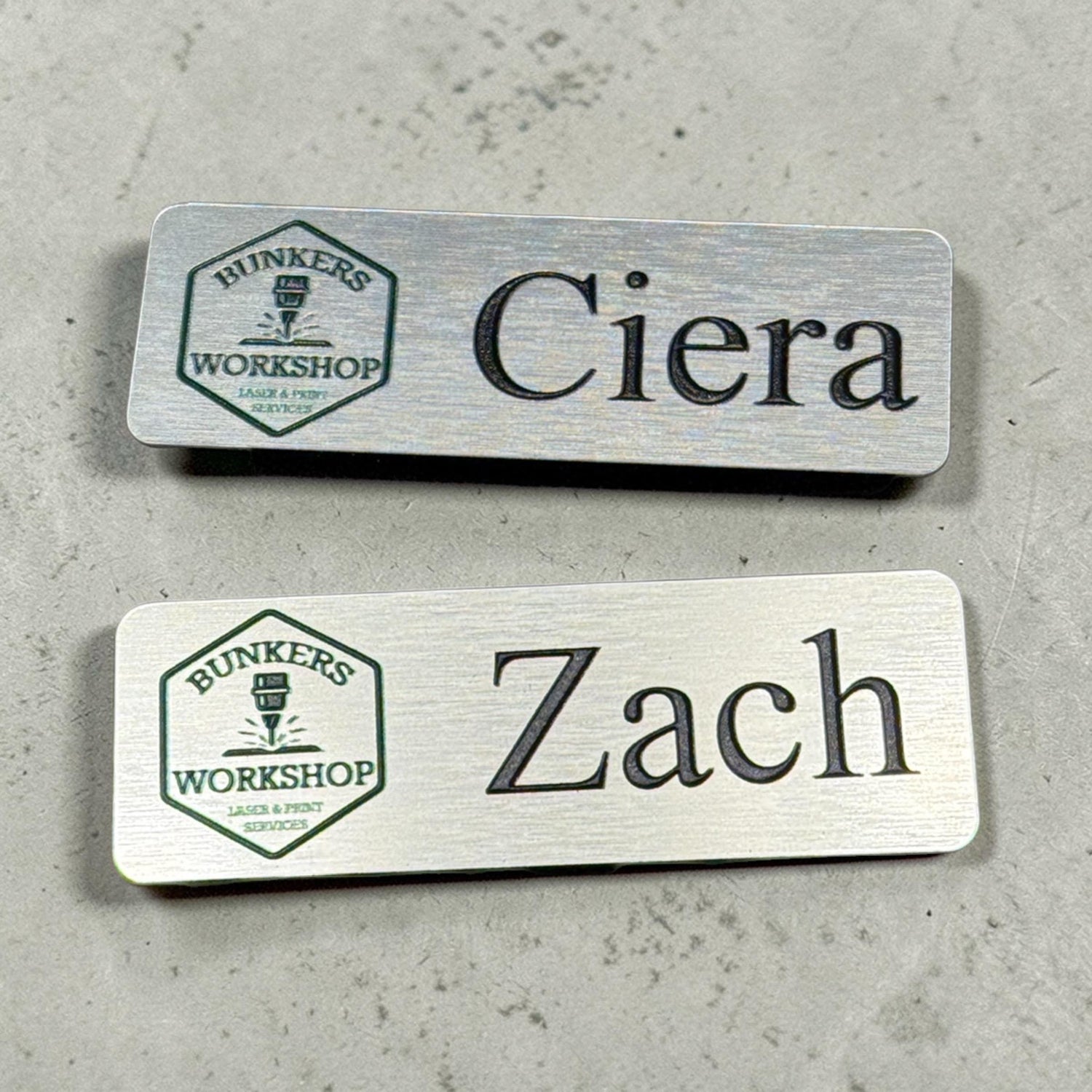 Brushed silver metal name badge with personalized logo and magnetic or pin back, designed for employees by Bunkers Workshop